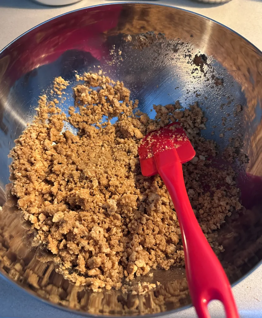 Graham cracker crumbs and melted butter in a mixing bowl with a rubber spatula.
