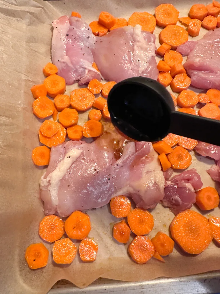 A spoon pouring some honey-garlic soy sauce onto some raw chicken thighs on a baking sheet.