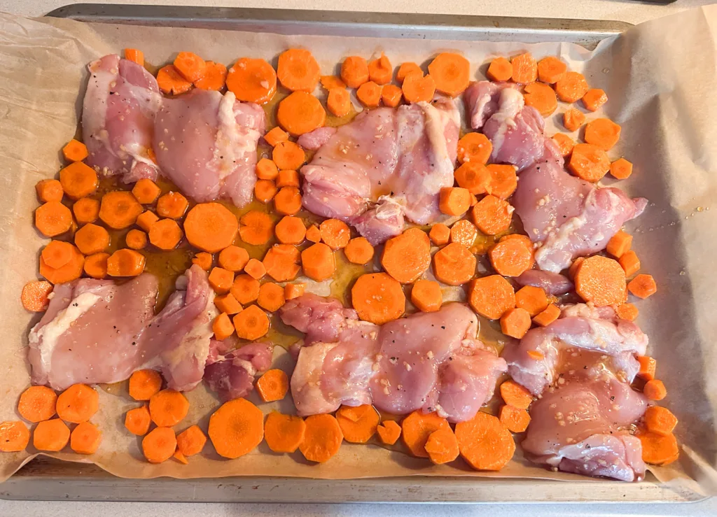 Chicken thighs next to carrots, still raw before going into the oven.