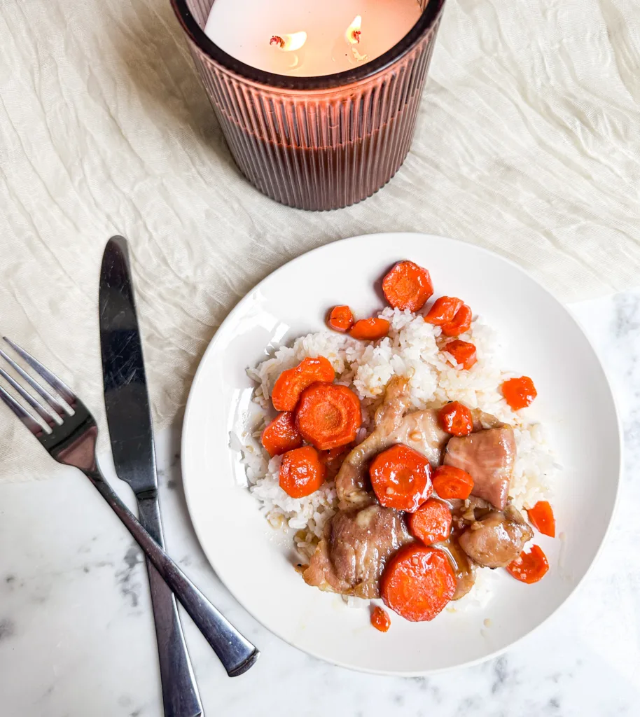 Honey garlic chicken thighs on a plate of rice, next to a butter knife and fork and a candle.