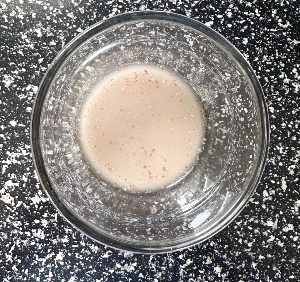 Water and ground flax seed in a glass bowl on a counter.