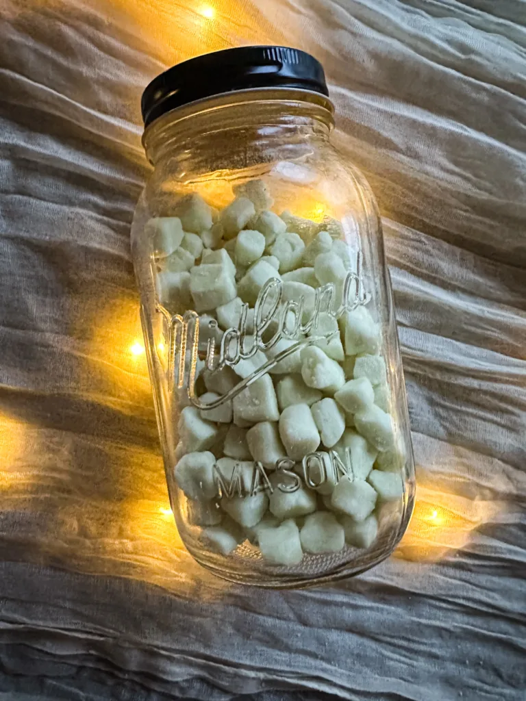 A glass mason jar full of butter mints on top of a table cloth with lights.