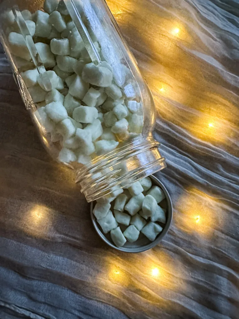 Butter mints in a glass mason jar and in a lid on a table cloth with lights.