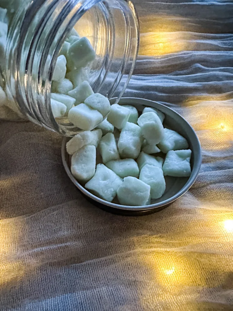 A jar of butter mints pouring out into a lid on top of a table cloth with lights.