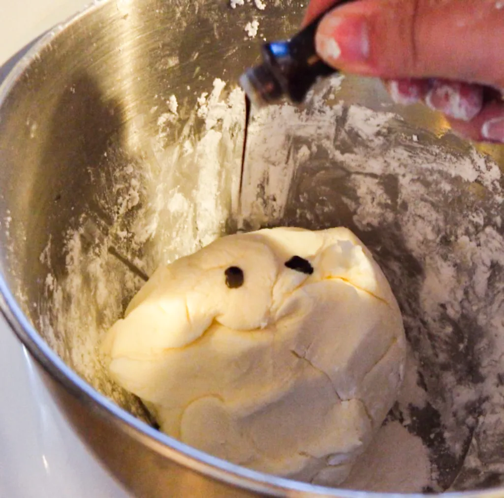 A hand adding a few drops of food coloring to butter mint dough.
