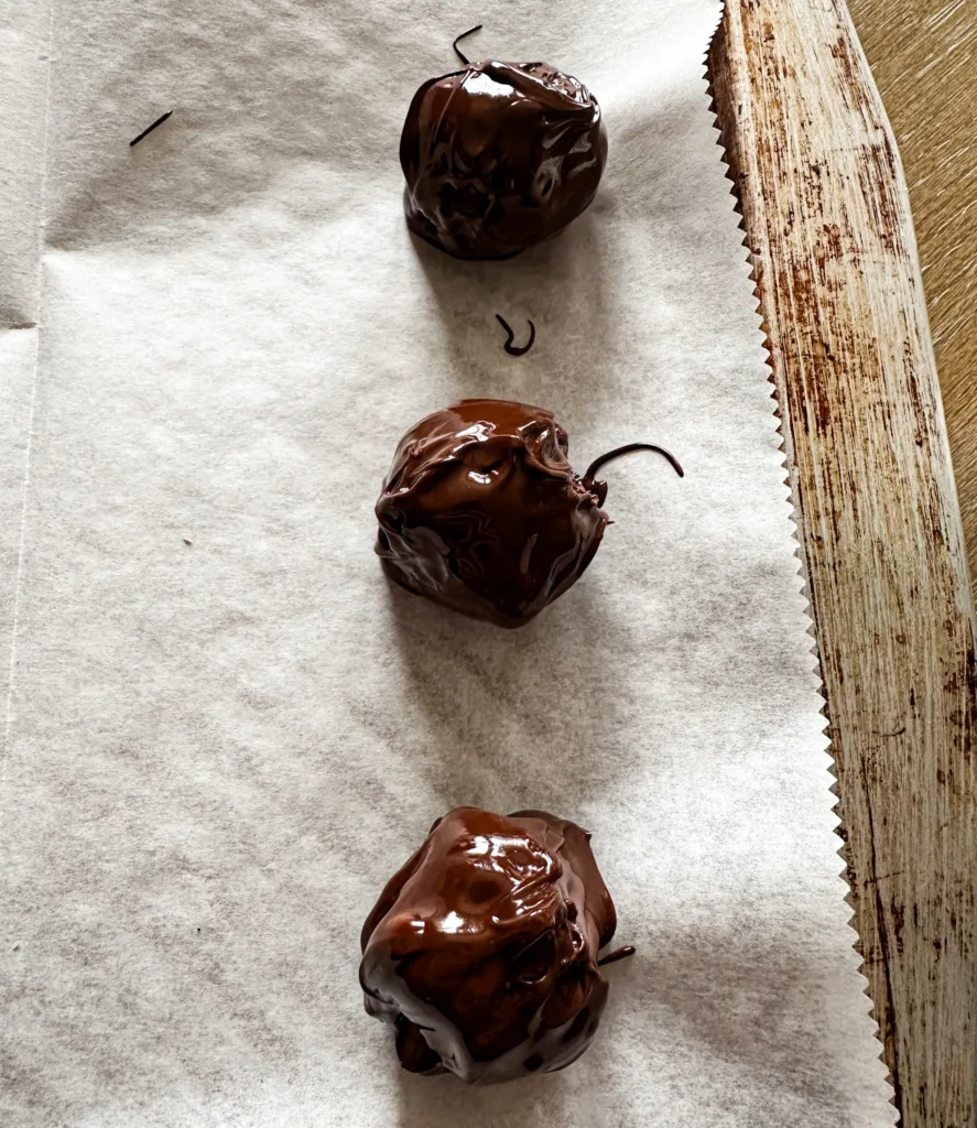 Three chocolate date balls on parchment paper on a baking sheet.