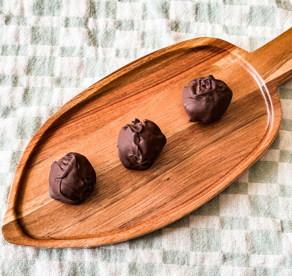 Chocolate date balls on a wooden board sitting on top of a tea towel.