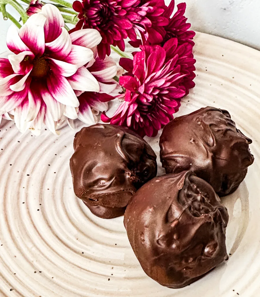 Chocolate date balls on a plate next to pink and white flowers.