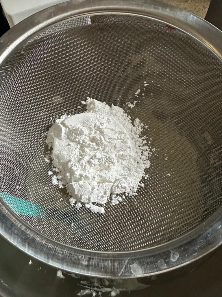 Powdered sugar being added into the cream cheese and butter mixture.