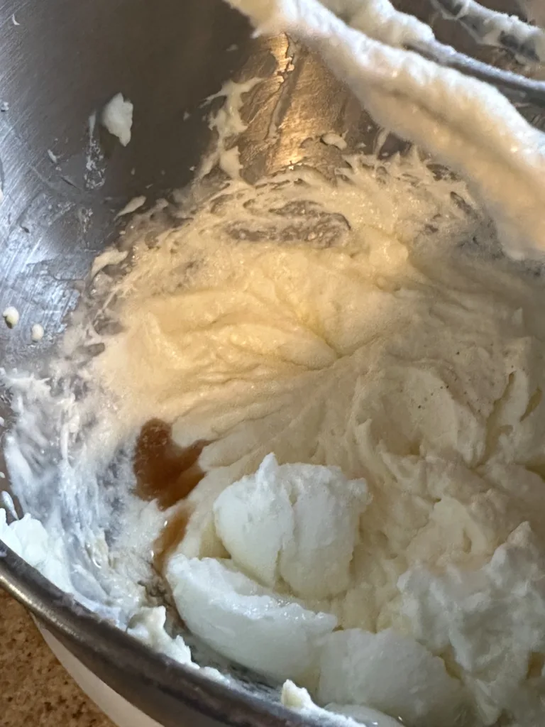 Vanilla extract added into a cream cheese, butter mixture in a stand mixer bowl.
