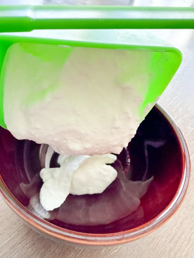 A measuring cup adding sour cream to a bowl.