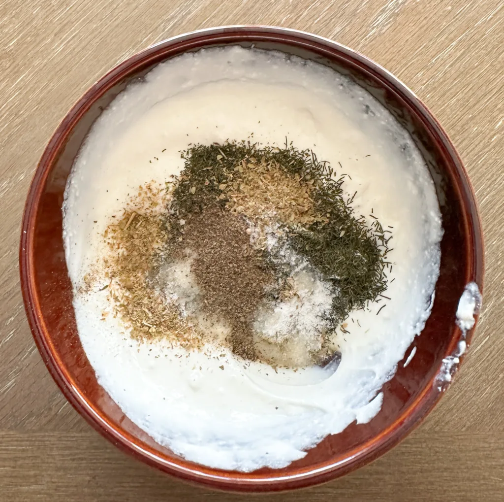 Sour cream and oregano, dill weed, garlic salt, and pepper in a bowl.