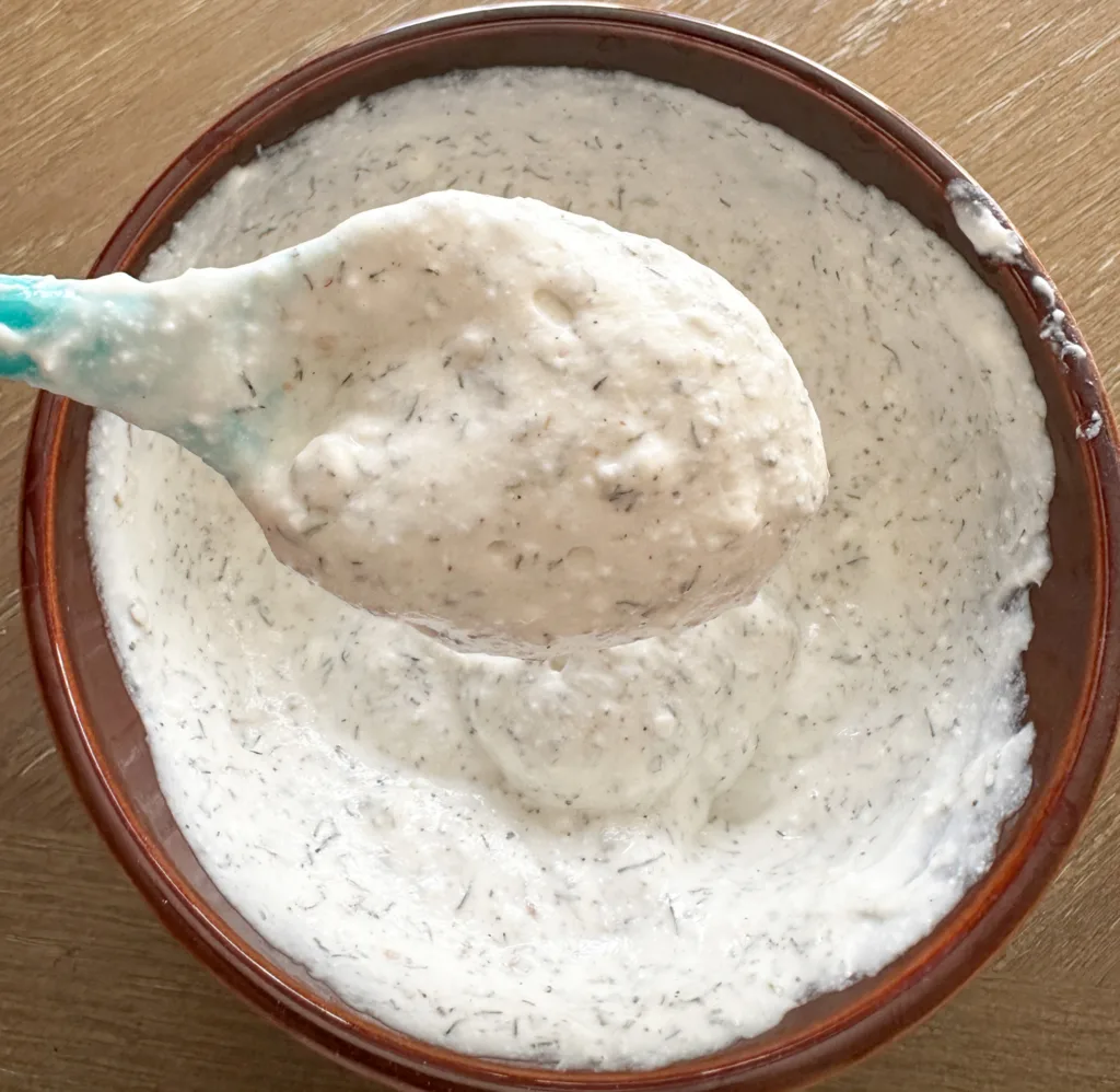 A spoon holding up some dip, over a bowl with dip in it.