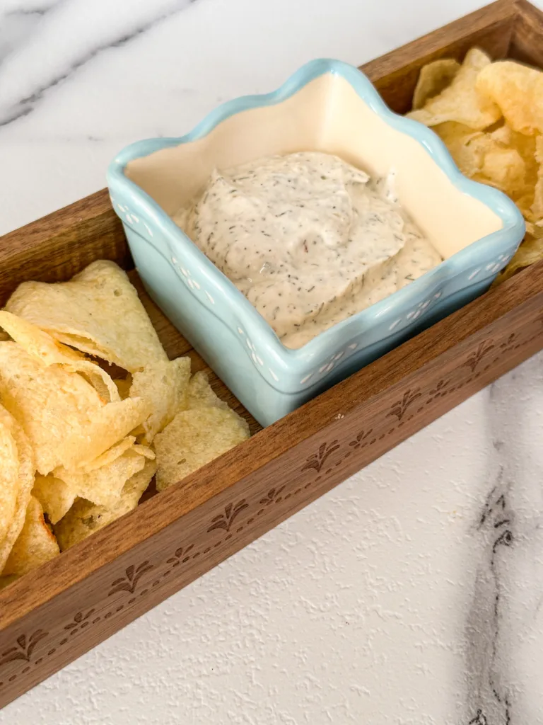 A bowl of dip in the middle of a wooden tray of potato chips.