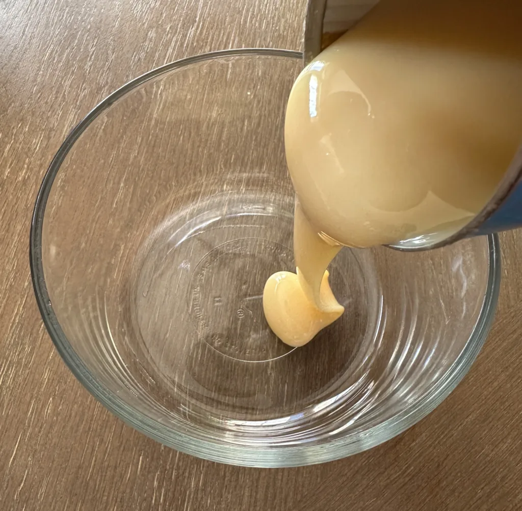 Pouring sweetened condensed milk into a glass bowl.