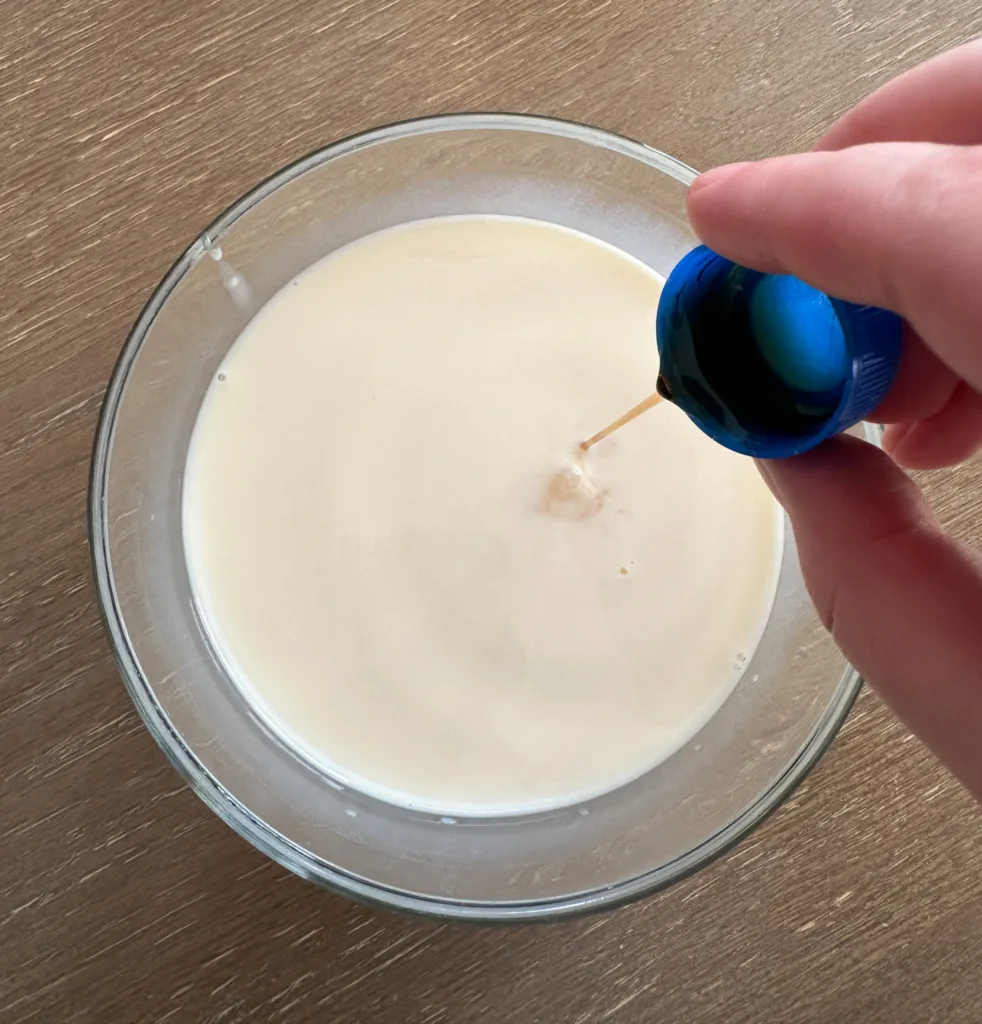 Vanilla being poured into a bowl of milk.