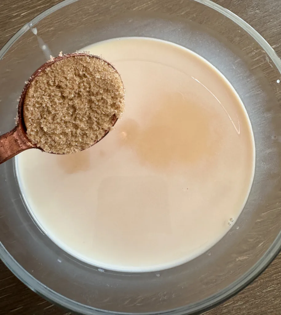 Brown sugar being added to a bowl of milk.