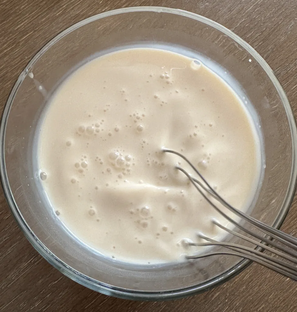 A whisk inside of a glass bowl of milk.