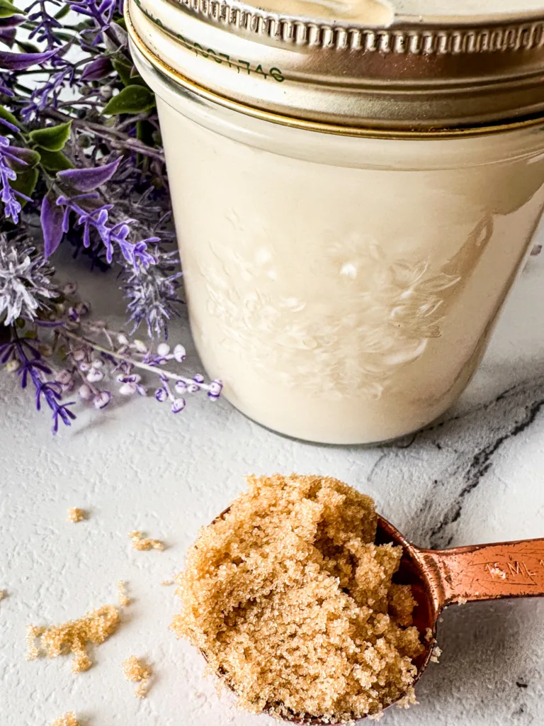 A jar of homemade coffee creamer next to some lavender and a measuring spoon full of brown sugar.