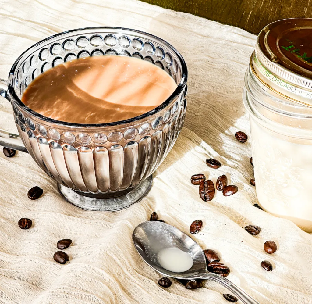 A cup of coffee next to homemade coffee creamer and some coffee beans.