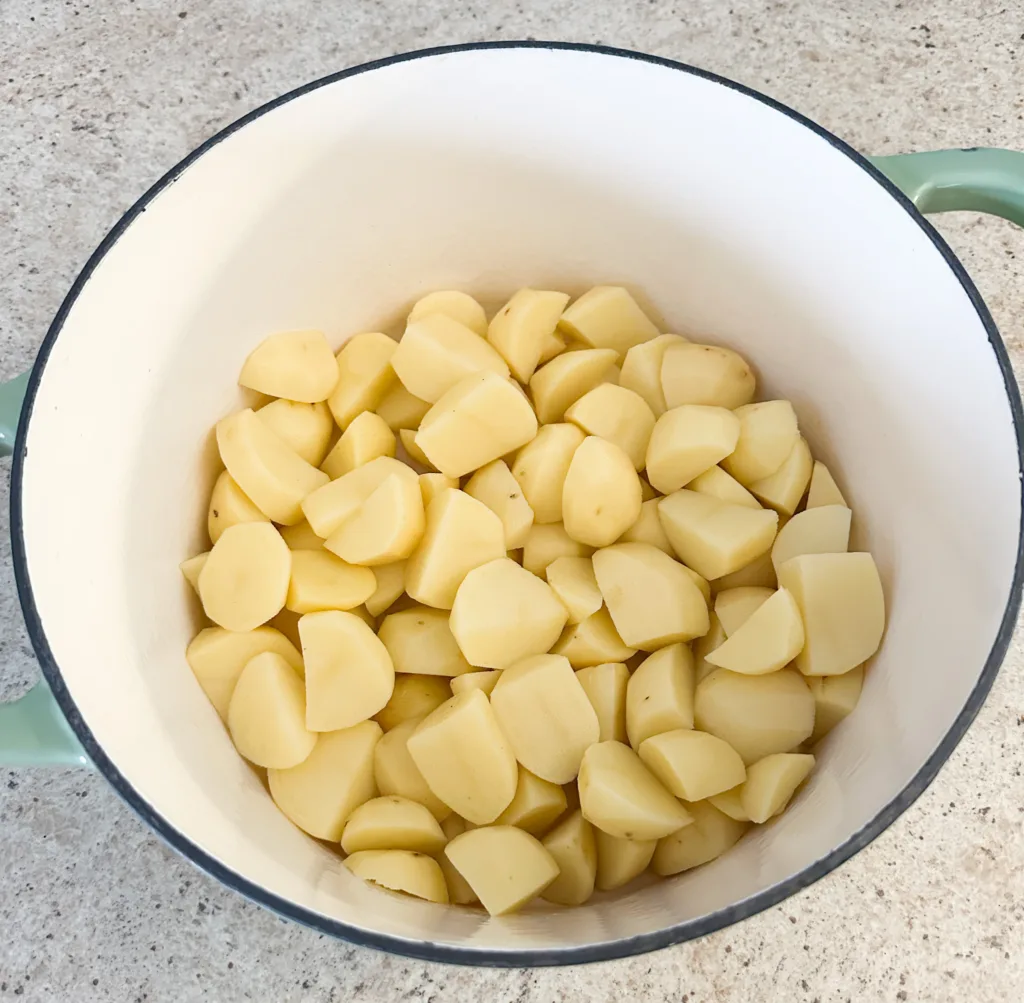 A pot of potatoes that are peeled and cubed.