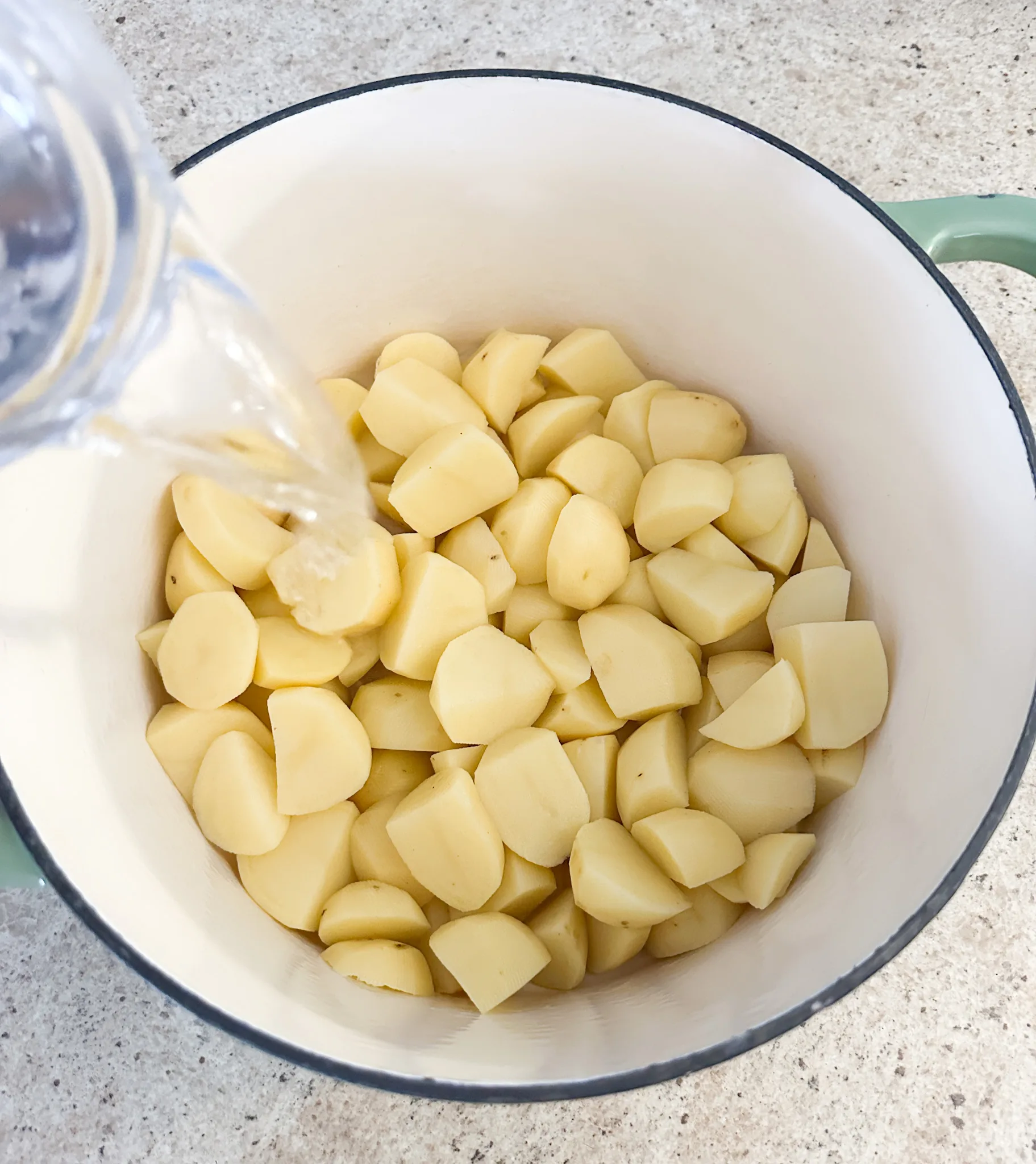 Water being poured into a pot of potatoes that are peeled and cubed.