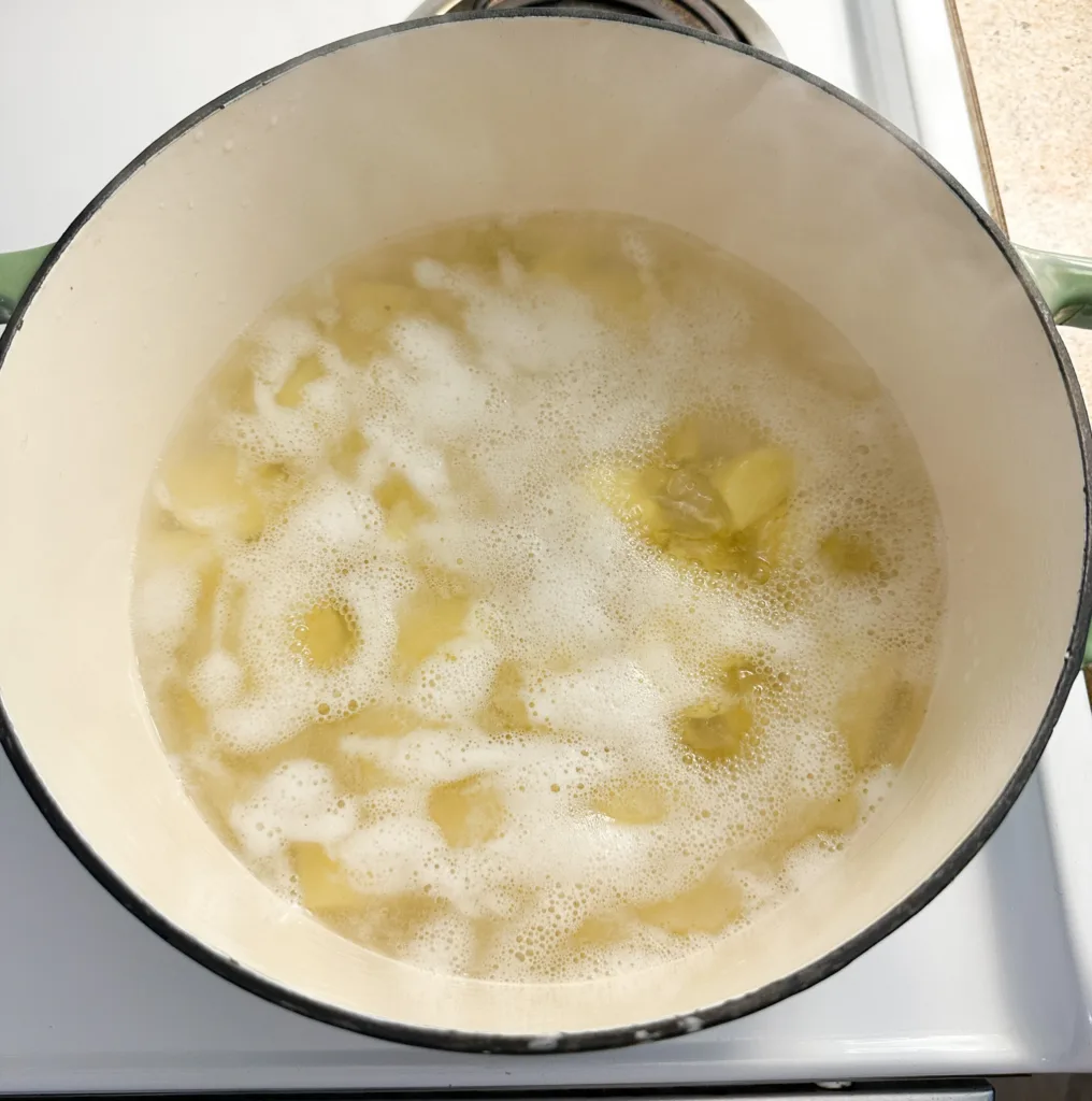 A pot of peeled and cubed potatoes boiling on a stove top.