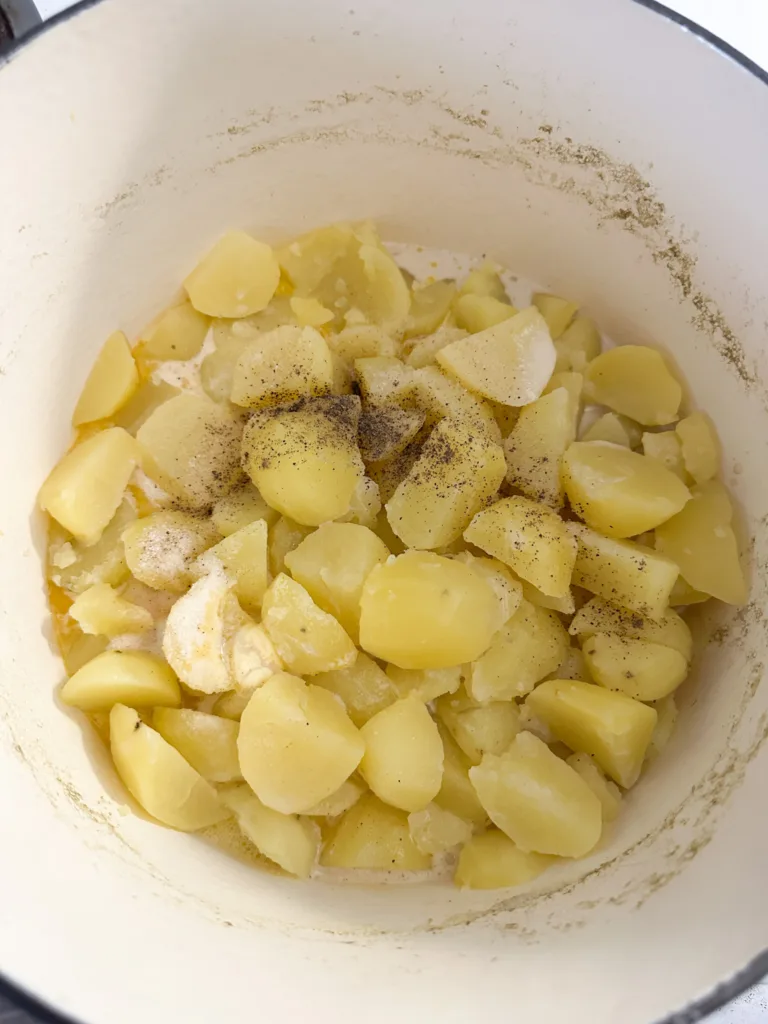 A pot of potatoes that are cubed, peeled, and boiled with plant-based butter, oat milk, and seasonings on them.