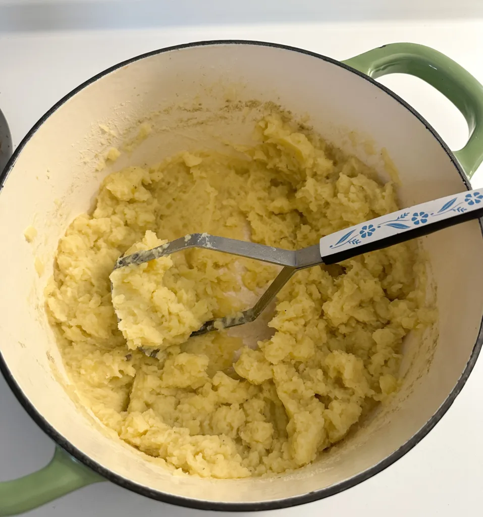 Mashed potatoes in a pot with a potato masher.