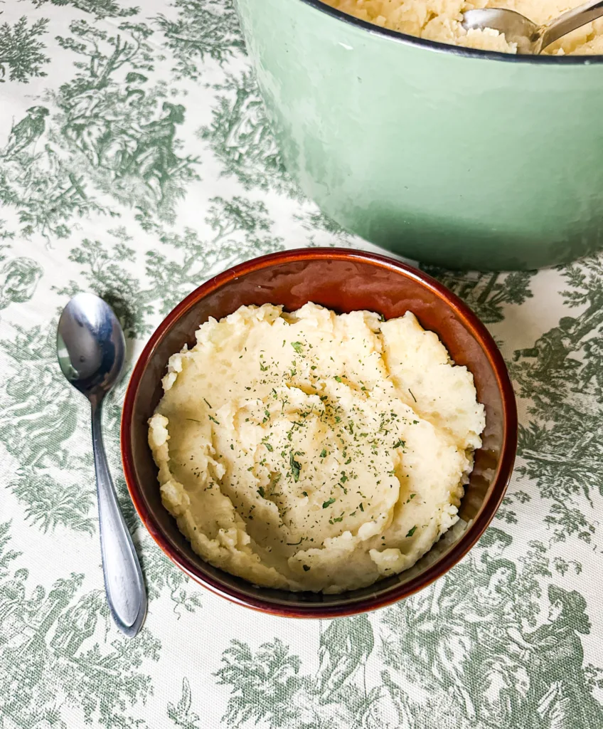 Dairy-free mashed potatoes in a bowl next to a pot and a spoon.