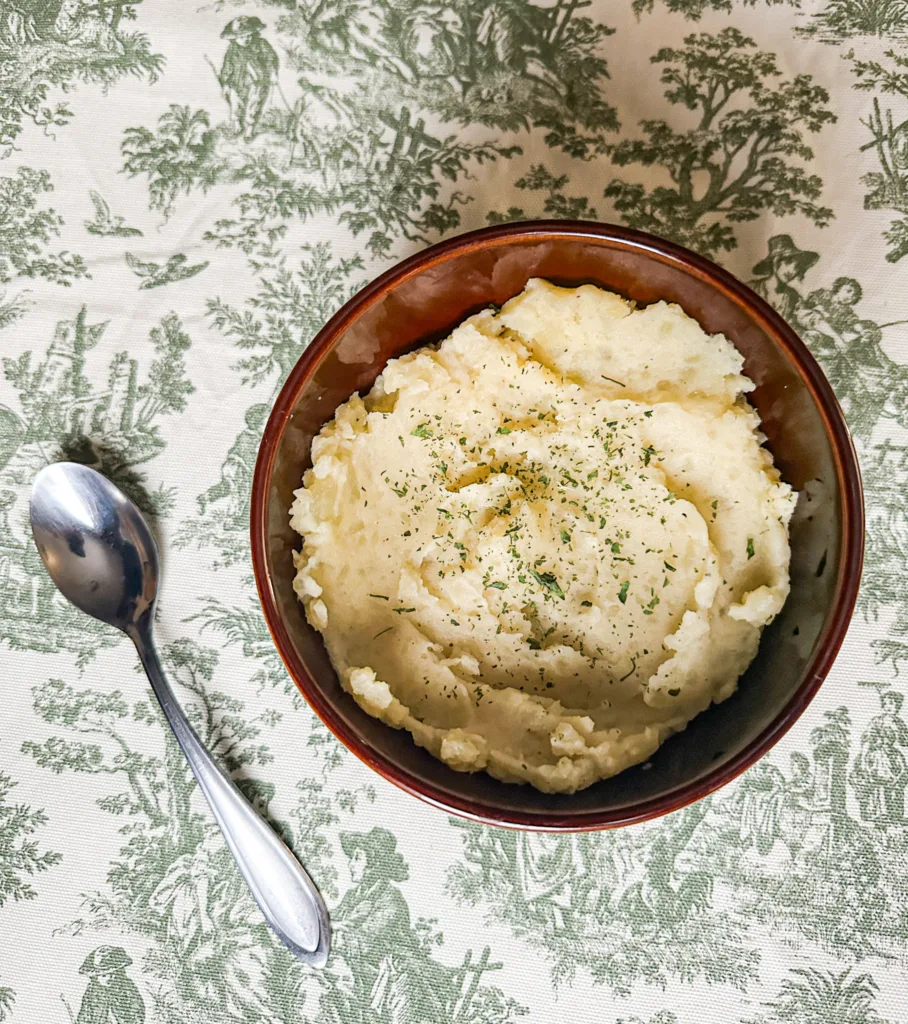 Dairy-free mashed potatoes in a bowl, next to a spoon and on a table cloth.