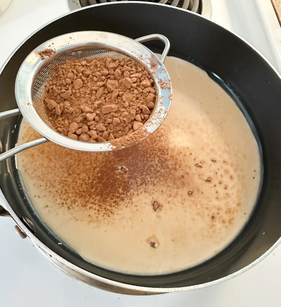 Cocoa powder being added to a pan with maple syrup and milk.