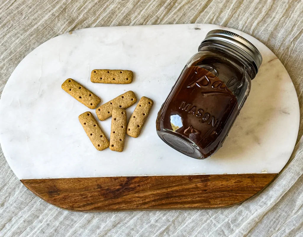 A jar of my chocolate sauce recipe next to some graham crackers on top of a cutting board.