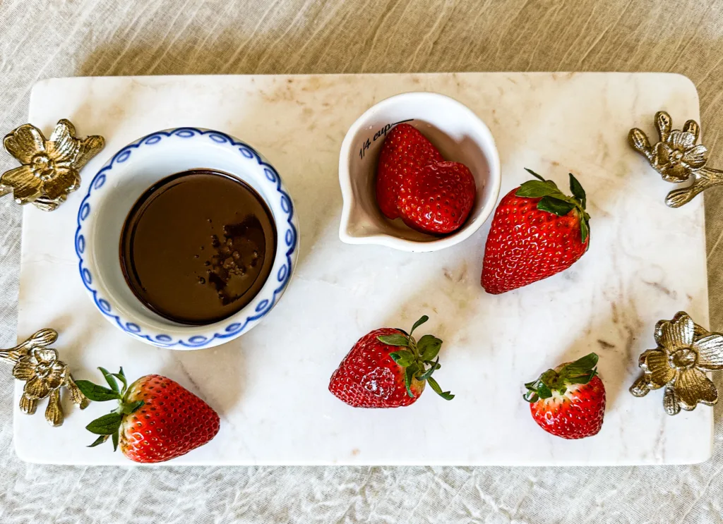 My chocolate sauce recipe in a bowl, on a cutting board, next to some strawberries.