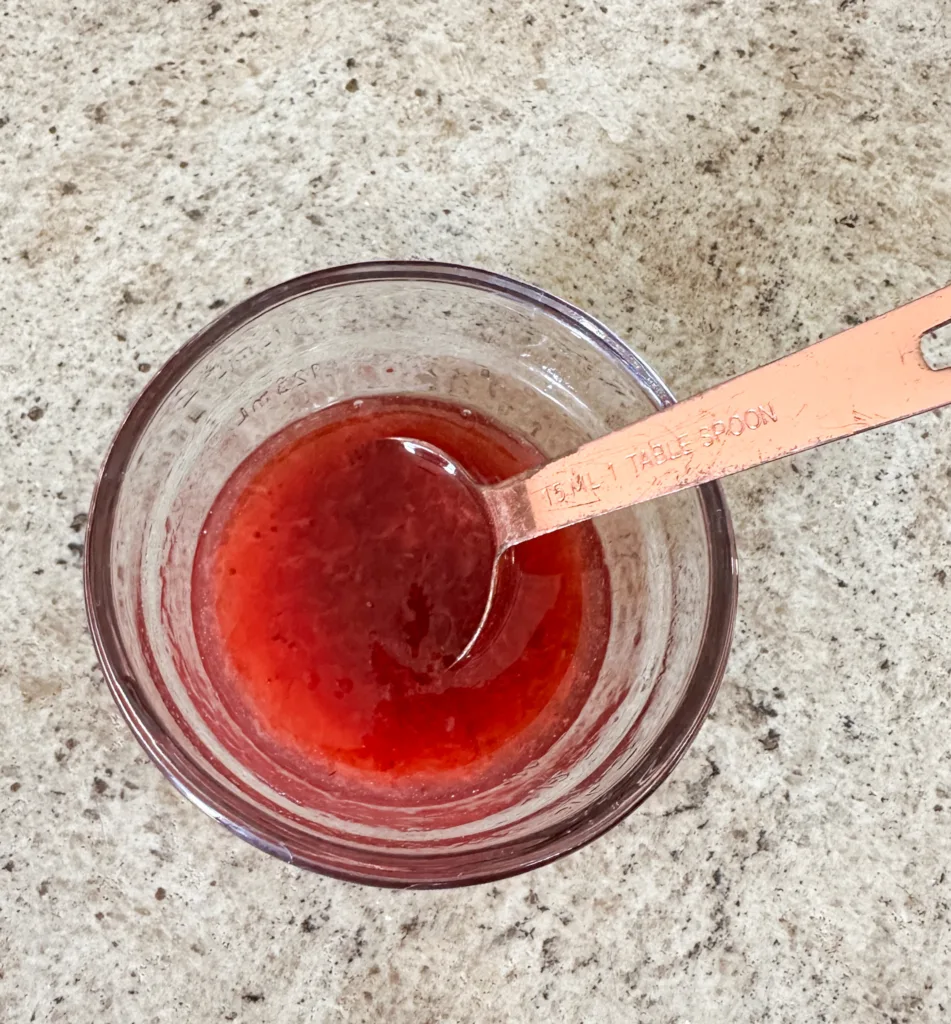 Strawberry syrup in a glass bowl with a measuring spoon.