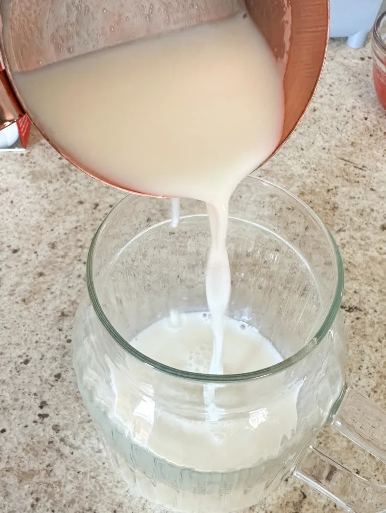 Milk being poured into a glass cup from a measuring cup.