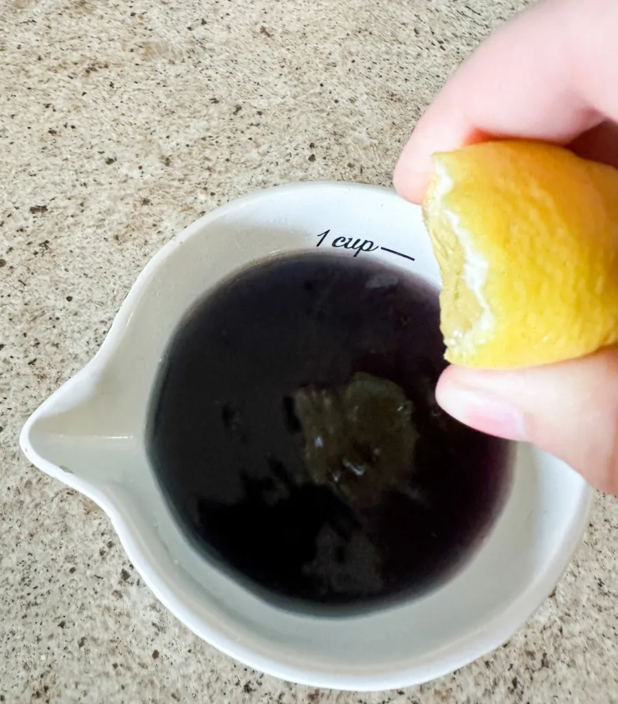 A lemon being squeezed into a cup of blue tea.
