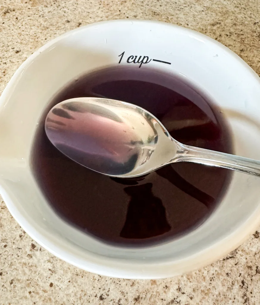 A spoon held up over a cup with purple tea in it.