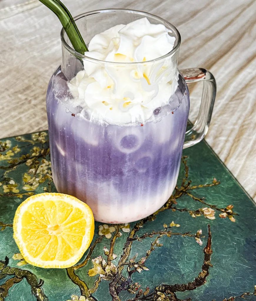 Butterfly pea tea latte on a decorative cutting board with half of a lemon.