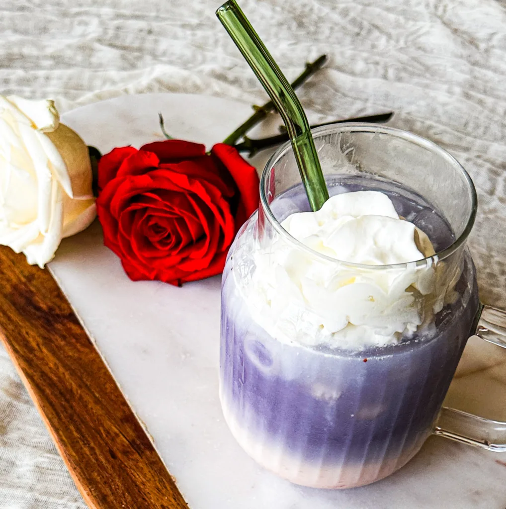 A butterfly pea tea latte on a cutting board next to some roses.
