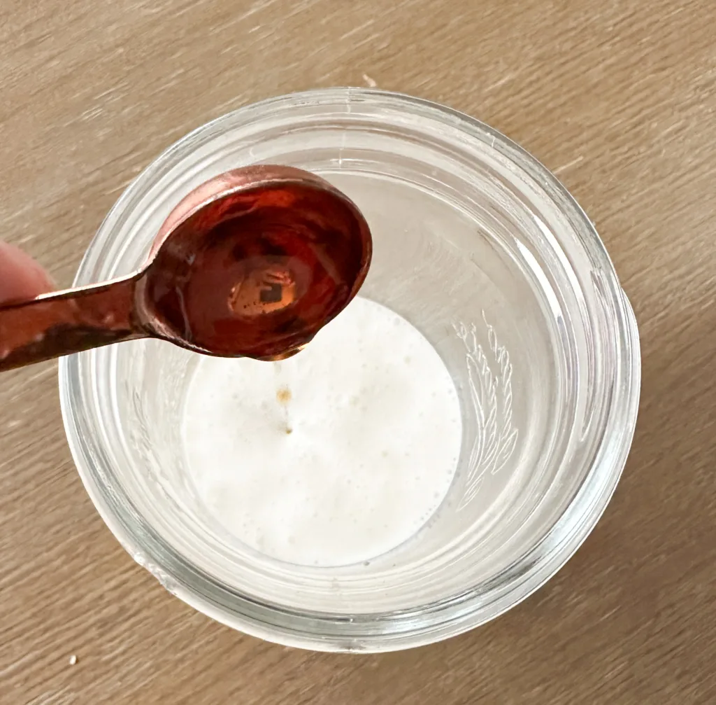 Syrup being poured into a glass cup with heavy whipping cream and milk.