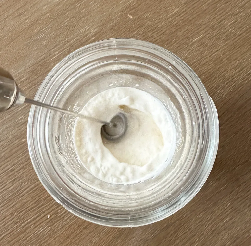 A frother frothing some cold foam in a glass cup.