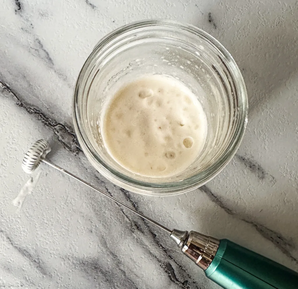Cold foam in a cup next to a milk frother,