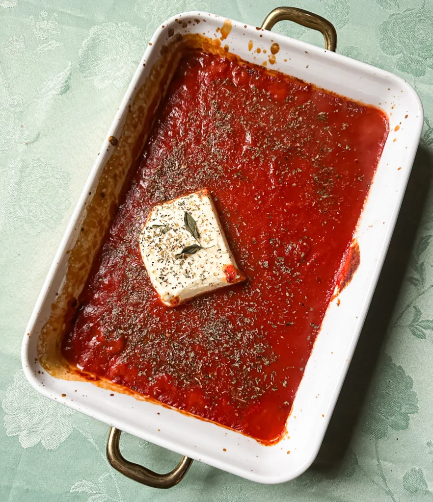 Cream cheese pasta sauce in an oven-safe baking pan, fresh out of the oven with half a block of cream cheese in the middle.