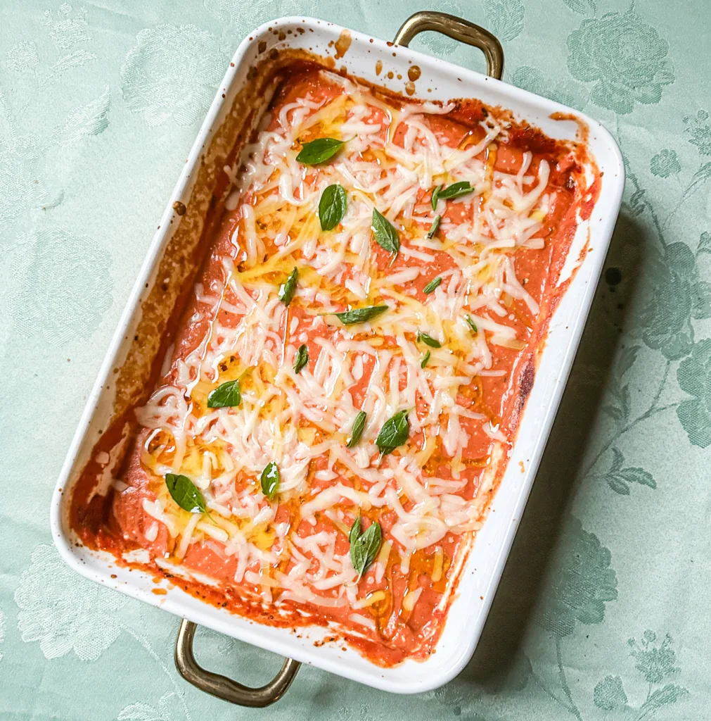 Cream cheese pasta sauce in a oven-safe baking pan with olive oil, cheese, and oregano.