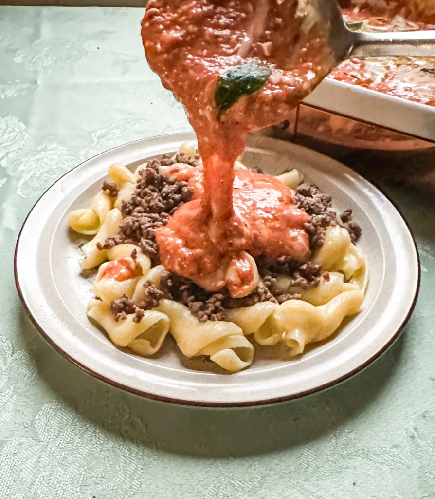 Cream cheese pasta sauce being poured onto ground beef and noodles.