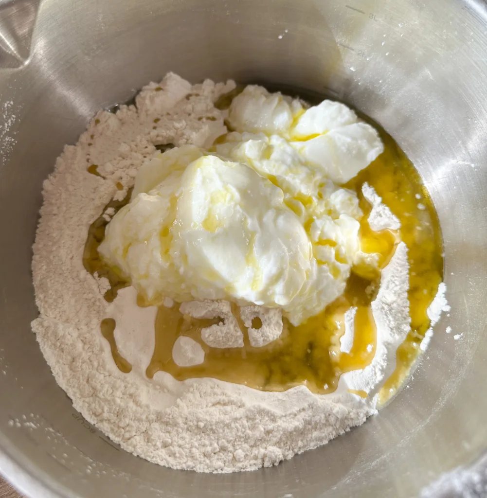 A mixing bowl with flour, yogurt, and olive oil.