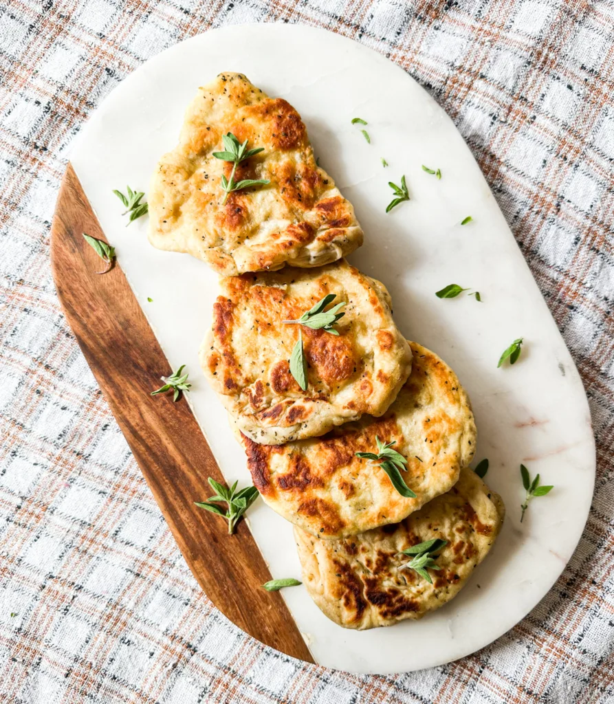 A homemade naan recipe on a marble cutting board with fresh oregano.