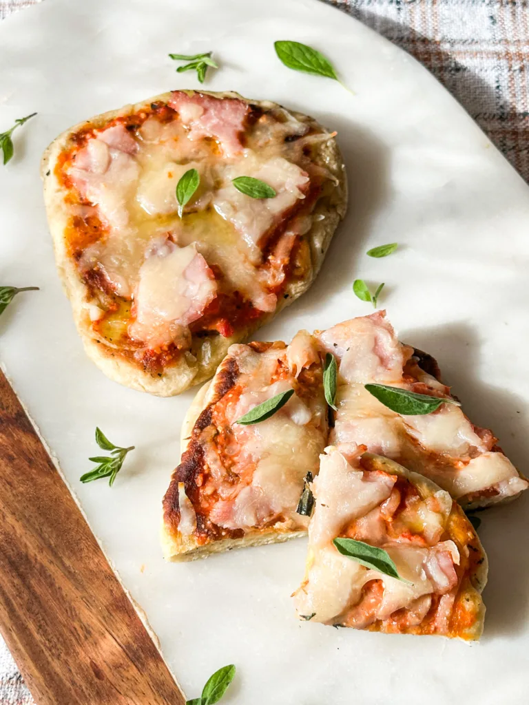 Homemade naan recipe pizzas on a cutting board with fresh oregano.