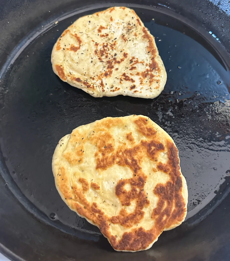 Two pieces of flat bread in a cast iron skillet.